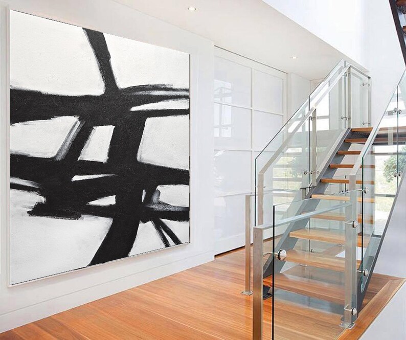 May include: Abstract black and white painting on a white canvas. The painting features bold black lines and shapes against a white background. The painting is hanging on a white wall in a modern home.