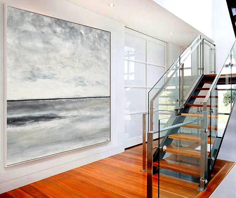 May include: A large abstract painting of a seascape in shades of gray and white. The painting is hanging on a white wall in a modern home with a glass staircase in the background.