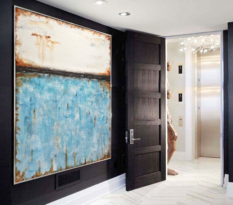 May include: Abstract painting with a white, brown, and blue color scheme. The painting is framed and hanging on a black wall in a hallway.