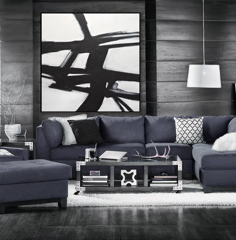 May include: A dark gray sectional sofa with a white and black geometric throw pillow. The sofa is in a living room with a black and white abstract painting on the wall and a coffee table with books and a decorative antler.