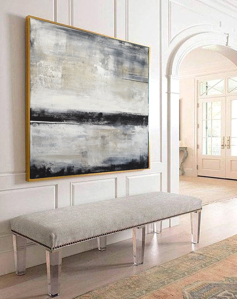 May include: Abstract art painting in a gold frame, featuring a blend of gray, black, and white brushstrokes. A gray upholstered bench with clear acrylic legs sits below the artwork. The scene is set in a well-lit hallway.