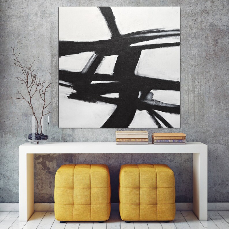 May include: A black and white abstract painting hangs above a white console table with two yellow cube ottomans. The painting features bold black lines and shapes on a white background.