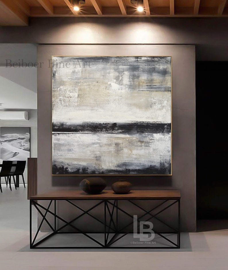 May include: Abstract landscape painting with a gold frame. The artwork features a textured surface with a palette of white, gray, and black. The painting is displayed above a wooden console table with two decorative vases.