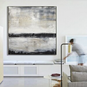 May include: Large abstract painting with a black frame. The artwork features a textured surface with a palette of white, gray, and black. Horizontal black lines and brushstrokes create a sense of depth and movement. The painting is displayed on a white wall.