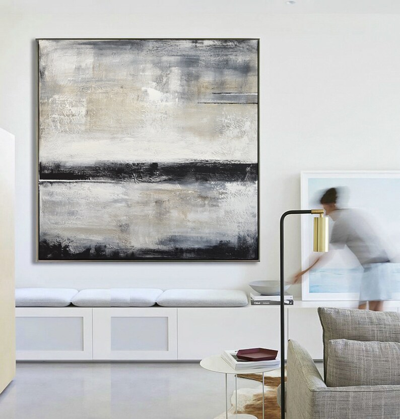 May include: Large abstract painting with a black frame. The artwork features a textured surface with a palette of white, gray, and black. Horizontal black lines and brushstrokes create a sense of depth and movement. The painting is displayed on a white wall.