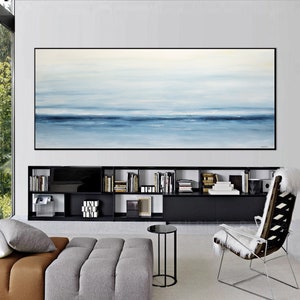 May include: A large abstract painting of a seascape in shades of blue and white hangs above a black bookshelf in a modern living room. The painting is framed in black and has a subtle texture.