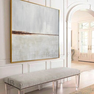 May include: A large abstract painting with a horizontal brown line across the middle, framed in gold, hangs above a white bench with clear acrylic legs. The bench is in a white room with a doorway leading to another room.