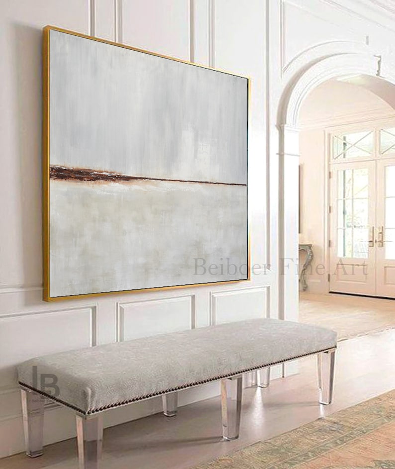 May include: A large abstract painting with a horizontal brown line across the middle, framed in gold, hangs above a white bench with clear acrylic legs. The bench is in a white room with a doorway leading to another room.