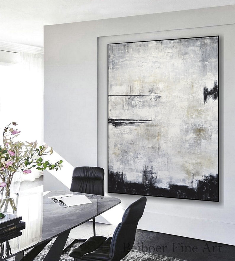 Op de afbeelding: Groot abstract schilderij met zwarte lijst. Het kunstwerk toont een textuurontwerp in tinten wit, grijs en zwart. Het heeft een horizontale zwarte lijn en een zwarte basis. De stijl is modern en minimalistisch, geschikt voor moderne interieurs.