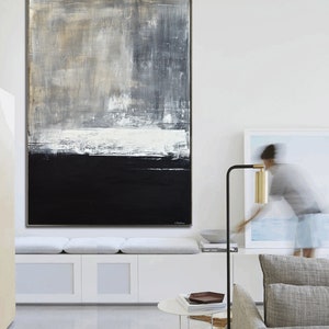 May include: Abstract painting with a black, white, and gray color scheme. The painting is hung on a white wall in a modern living room.