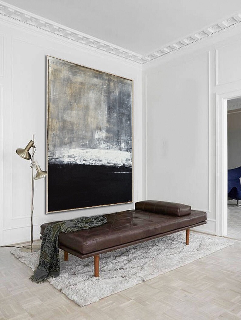 May include: A large abstract painting with shades of gray, white, and black hangs on a white wall above a brown leather daybed. The daybed is on a white shag rug in a room with white walls and a white ceiling.