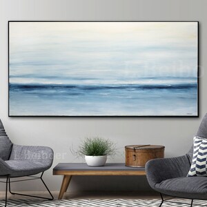 May include: Abstract painting of a seascape with shades of blue and white. The painting is framed in a black frame and hangs on a white wall.