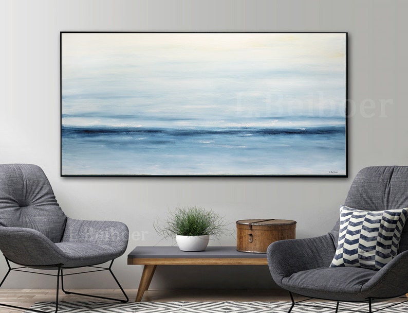May include: Abstract painting of a seascape with shades of blue and white. The painting is framed in a black frame and hangs on a white wall.
