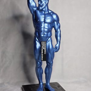 May include: A metallic blue sculpture of a muscular male figure, posed with one arm raised. The statue has a beard and is standing on a black rectangular base. The text "MODERN MYTHOS.COM" is partially visible on the figure.
