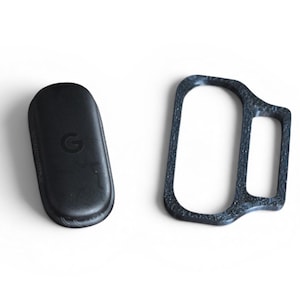 May include: Two black tech accessories are displayed on a white background. One is a rounded rectangle with a 'G' logo, and the other is a dark gray, textured frame. The items appear to be related to technology or electronics.
