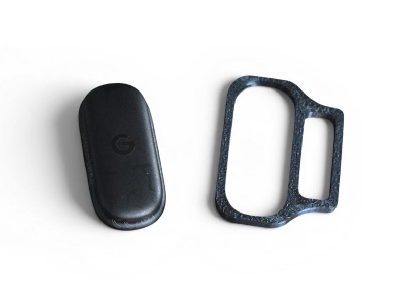 May include: Two black tech accessories are displayed on a white background. One is a rounded rectangle with a 'G' logo, and the other is a dark gray, textured frame. The items appear to be related to technology or electronics.