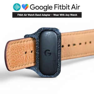May include: A close-up of a Google Fitbit Air watch band adapter. The adapter is black with a speckled texture and a leather watch band. The Google logo is visible on the adapter. The text "Fitbit Air Watch Band Adapter - Wear With Any Watch" is also visible.