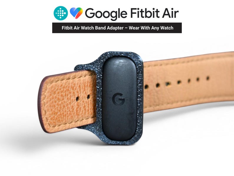 May include: A close-up of a Google Fitbit Air watch band adapter. The adapter is black with a speckled texture and a leather watch band. The Google logo is visible on the adapter. The text "Fitbit Air Watch Band Adapter - Wear With Any Watch" is also visible.
