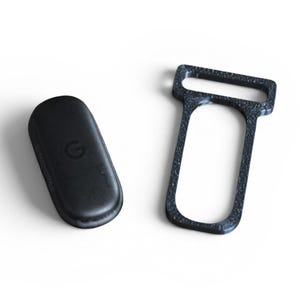 May include: Two black objects on a white background. One is a rounded rectangle with a debossed "G" logo. The other is a dark gray, textured, rectangular frame with a large opening.