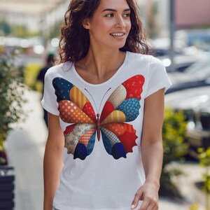 以下が含まれることがあります： カラフルな蝶のデザインが施された白いTシャツ。蝶の羽は、赤、青、オレンジ、黄色のさまざまな模様のパッチで構成されています。Tシャツは丸首で半袖です。