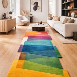 Op de afbeelding: Een selectie van kleurrijke geometrische tapijten in een moderne woonkamer. De tapijten hebben een verscheidenheid aan kleuren, waaronder oranje, rood, blauw, groen en geel. De tapijten zijn rechthoekig en hebben een geometrisch ontwerp. De kamer heeft houten vloeren en witte muren.
