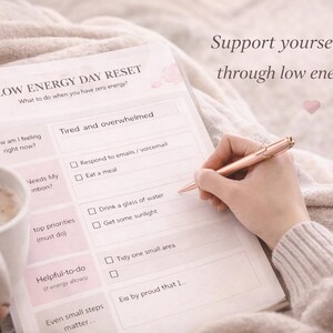 May include: A pale blanket forms the background for a "LOW ENERGY DAY RESET" checklist. A hand with a rose gold pen is writing on the list. A mug of coffee is also present. The text reads "Support yourself gently through low energy days."