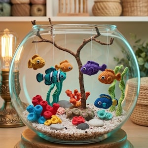 Könnte beinhalten: Dekoratives Glasfischbecken mit Holzsockel, gefüllt mit kleinen Steinen und farbenfrohen gehäkelten Korallen und Seetang. Gehäkelte Fische in Gelb, Orange, Blau und Lila hängen an einem Ast im Inneren des Beckens.