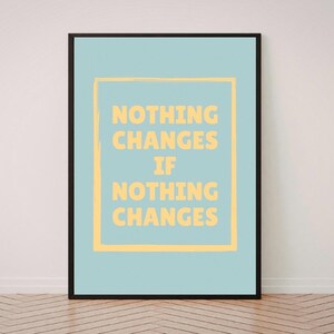 May include: A framed print with a light blue background and the text "NOTHING CHANGES IF NOTHING CHANGES" in yellow. The text is inside a yellow square. The frame is black.
