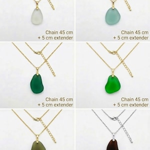 May include: A collection of necklaces with pendants in various colors, including white, teal, green, and brown. Each necklace features a gold-colored chain with a 45 cm length and a 5 cm extender. The pendants have a smooth, organic shape.