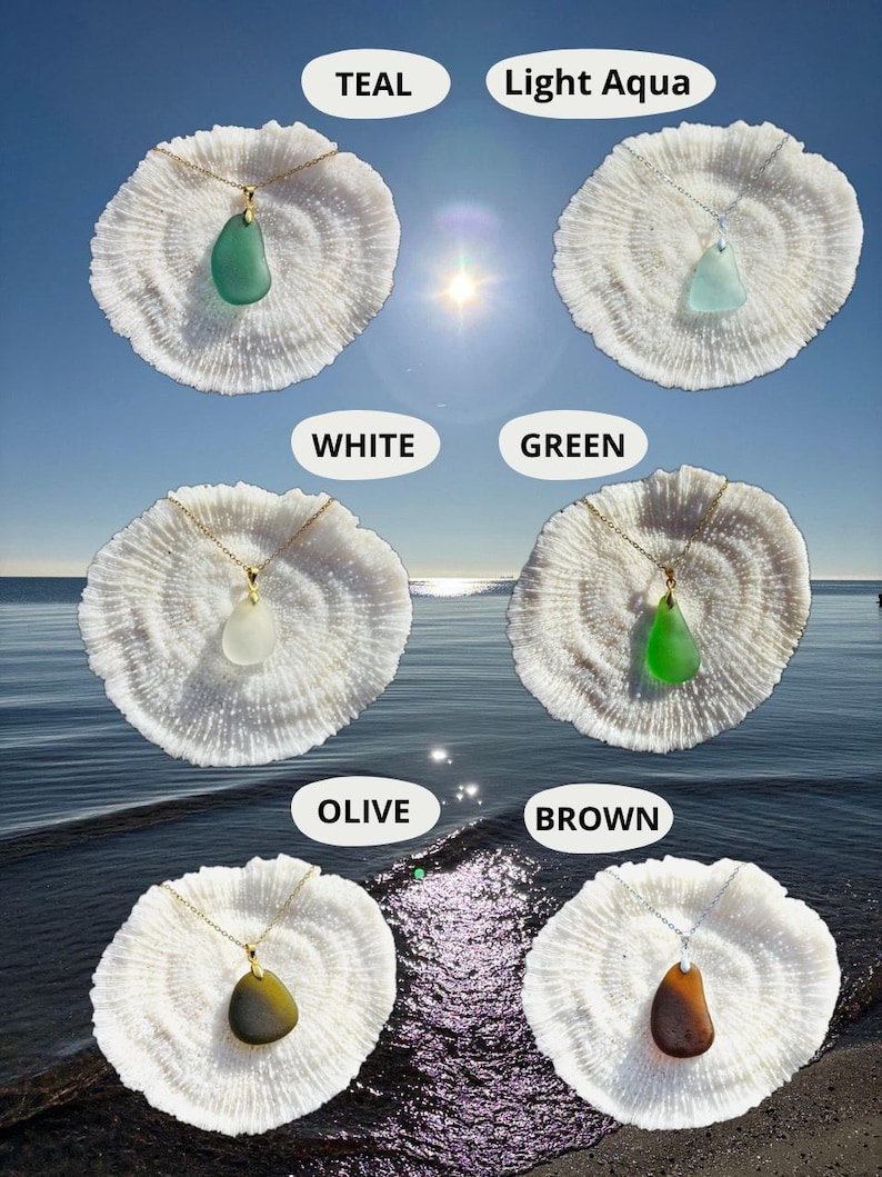 May include: Necklaces with sea glass pendants in various colors, including teal, light aqua, white, green, olive, and brown. Each pendant hangs from a delicate gold or silver chain and rests on a white coral-like base. The background shows a sunny sky and ocean.