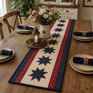 May include: A patriotic table setting featuring a cream-colored table runner with navy blue stars, red stripes, and a navy blue border. The table is set with plates, napkins, and a vase of flowers. A lit candle in a lantern adds ambiance.
