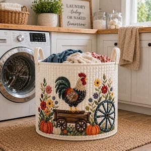 May include: Cream-colored, quilted laundry basket with a rooster and floral embroidery. The basket has two handles and is filled with folded clothes. The design includes pumpkins, a wagon wheel, and the text "LAUNDRY TODAY OR NAKED TOMORROW" on a sign in the background.