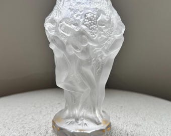 Pode incluir: Um vaso de vidro fosco com um design de relevo detalhado. O vaso apresenta figuras e cachos de uvas. A base tem uma faixa prateada com detalhes dourados. O design geral é elegante e artístico.