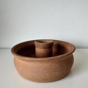 May include: A handmade, speckled, brown ceramic candle holder. The candle holder has a circular base with a raised center for the candle. The piece has a rustic, earthy aesthetic, perfect for home decor.