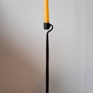 Puede incluir: Un candelero alto de hierro forjado con base en espiral y asa curva. La vela es una vela larga y cónica de cera de abeja amarilla. El candelero mide unos 40 cm de altura.