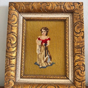 Peut inclure: Tableau de tapisserie vintage encadré représentant une femme en robe rouge, sur fond jaune. L'œuvre est encadrée dans un cadre en bois doré orné avec une bordure intérieure crème. Une pièce de décoration intérieure classique.