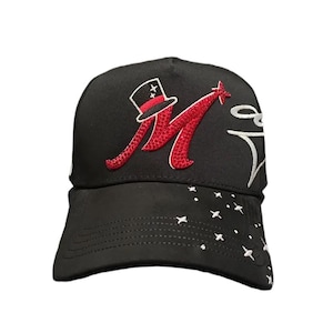 May include: Black baseball cap featuring a red embroidered letter "M" with a top hat and star design. The cap has a curved brim and white star accents. A white script design is on the right side.
