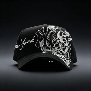 May include: Black baseball cap featuring white embroidered designs. The cap displays the New York Yankees logo and the words "New York" in script. A detailed skull graphic is on the side, adding a bold, edgy aesthetic to the headwear.