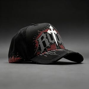 May include: Black baseball cap with a distressed brim. The cap features a white cross and the word "RUTH" in gray and red, with a splatter design. The hat is set against a dark gray background.