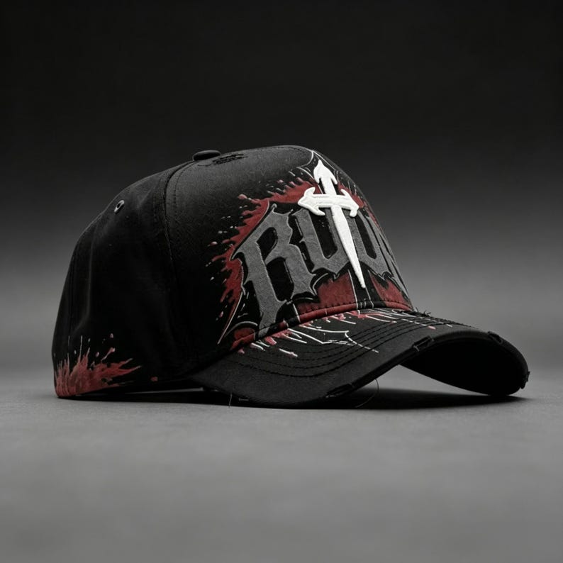 May include: Black baseball cap with a distressed brim. The cap features a white cross and the word "RUTH" in gray and red, with a splatter design. The hat is set against a dark gray background.