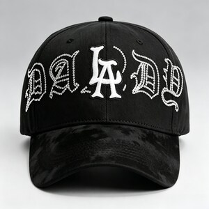 K&ouml;nnte beinhalten: Schwarze Baseballkappe mit dem Text "DA D" in Wei&szlig;, verziert mit Strasssteinen. Der Schirm hat ein dunkles, strukturiertes Muster. Die Kappe ist ein klassisches Sechs-Panel-Design.