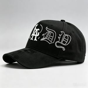 K&ouml;nnte beinhalten: Schwarze Baseballkappe mit wei&szlig;em Strass-Schriftzug "LA DB" in einer stilisierten Schriftart. Die Kappe hat einen gebogenen Schirm und einen Knopf oben. Der Hut ist aus strapazierf&auml;higem Stoff gefertigt.