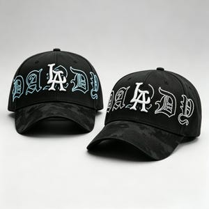 K&ouml;nnte beinhalten: Zwei schwarze Baseballkappen mit dem Wort "DADDY" in Wei&szlig; und Hellblau gestickt. Die Kappen haben ein Camouflagemuster auf Krempe und Krone. Die Kappen werden auf wei&szlig;em Hintergrund pr&auml;sentiert.