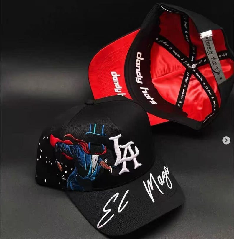 May include: Black baseball cap with a red satin lining and the text "dandy hats". The cap features an embroidered design of a magician with the text "LA" and "El Mago".