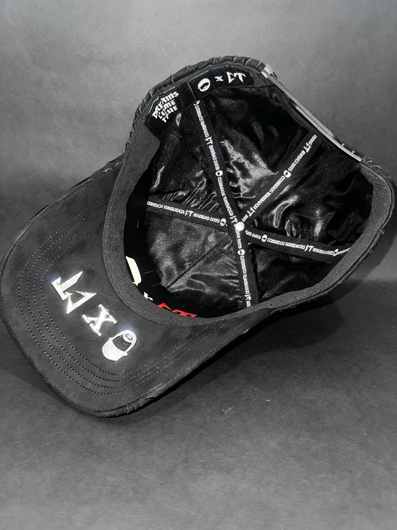 May include: Black baseball cap with the text "OXT" embroidered in white on the front. The cap features a curved brim and a satin lining. The text "DREAMS COME TRUE" is visible on the side.