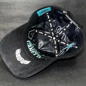 May include: Black baseball cap with white embroidered wing design on the side. The interior features a black lining with white text and a teal tag with the brand name. The cap has a curved brim.