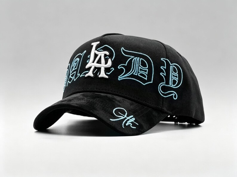 K&ouml;nnte beinhalten: Schwarze Baseballkappe mit den Buchstaben "LA" in Wei&szlig; und "D" in hellblauer Stickerei. Die Kappe hat einen gebogenen Schirm und eine strukturierte Krone. Der Text "9th" ist auf der Seite gestickt.
