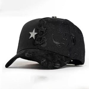 Può includere: Cappellino da baseball nero con visiera curva. Il cappellino presenta una stella ricamata e dettagli decorativi. È dotato di una chiusura in metallo sul retro per la regolazione. Un accessorio alla moda.