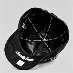 K&ouml;nnte beinhalten: Schwarze Baseballkappe mit wei&szlig;em Text "daunty hasts" auf der Vorderseite und "kanchy but the lessly eas istasy" im Inneren. Die Kappe hat einen gebogenen Schirm und ein Satinfutter.