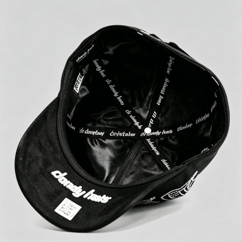 K&ouml;nnte beinhalten: Schwarze Baseballkappe mit wei&szlig;em Text "daunty hasts" auf der Vorderseite und "kanchy but the lessly eas istasy" im Inneren. Die Kappe hat einen gebogenen Schirm und ein Satinfutter.